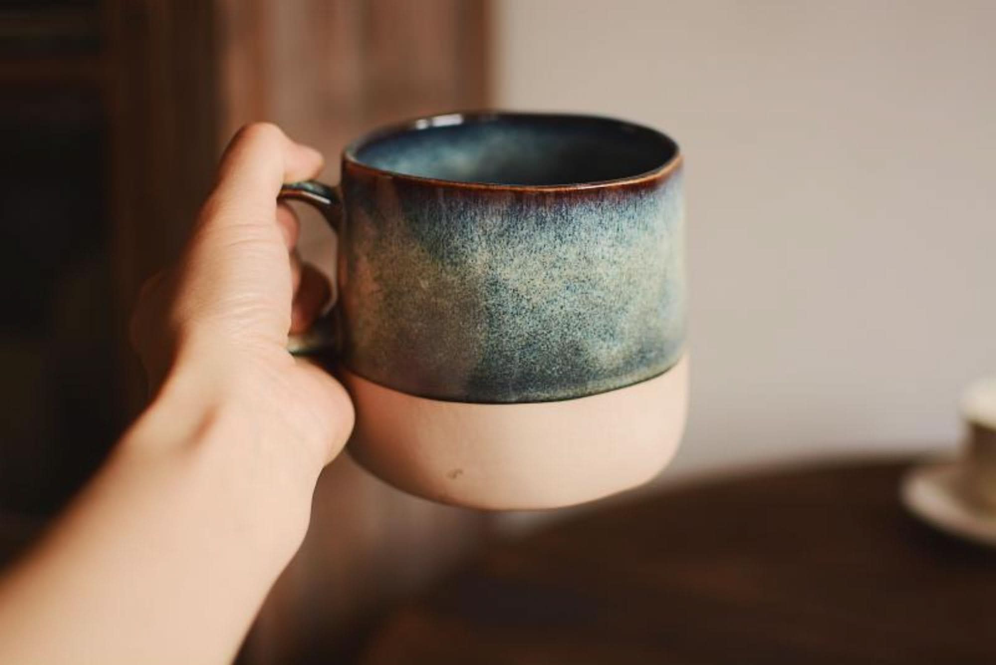 Reactive glazed pottery mug with blue-green gradient, held in hand.